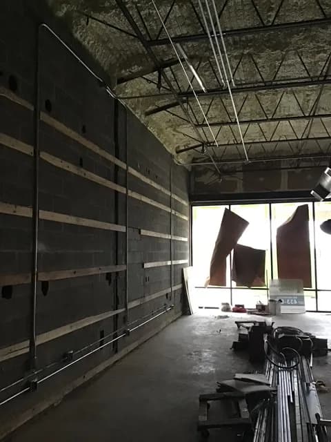Early-stage interior of the Australian Super Tans buildout — concrete block walls and overhead steel framing with structural conduit going up