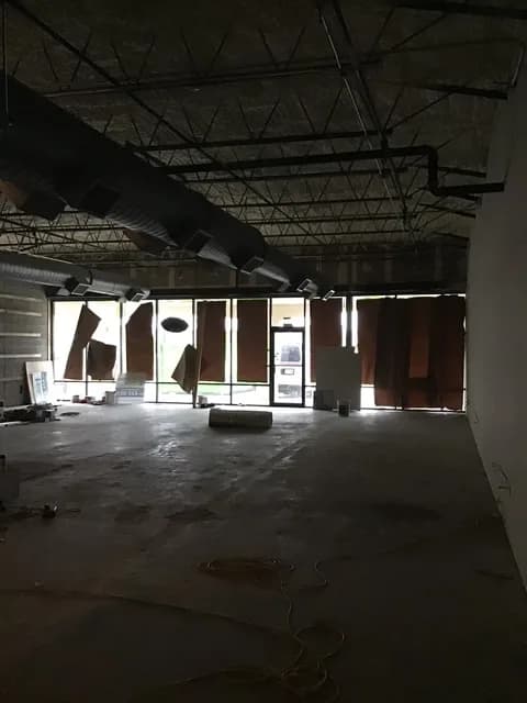 Wider interior view of the buildout with floor-to-ceiling storefront glass and HVAC + electrical infrastructure overhead