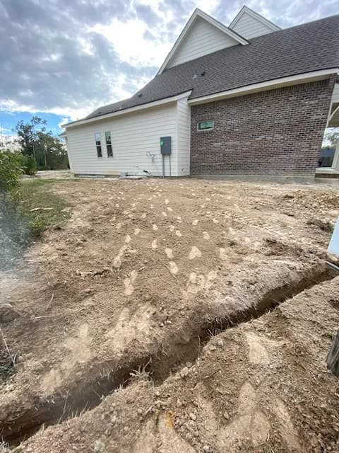 Side view of new-build brick-and-siding home with completed trench leading from house to pedestal